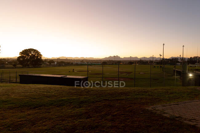 Paisaje del campo de béisbol y el campo circundante al amanecer. campo de béisbol vacío en idílica ubicación rural. - foto de stock