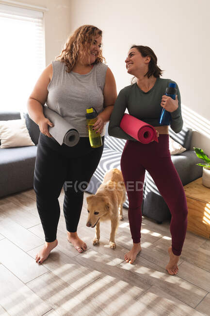 Lesbian couple practicing yoga, holding yoga mats smiling. domestic lifestyle, spending free time at home. — Stock Photo