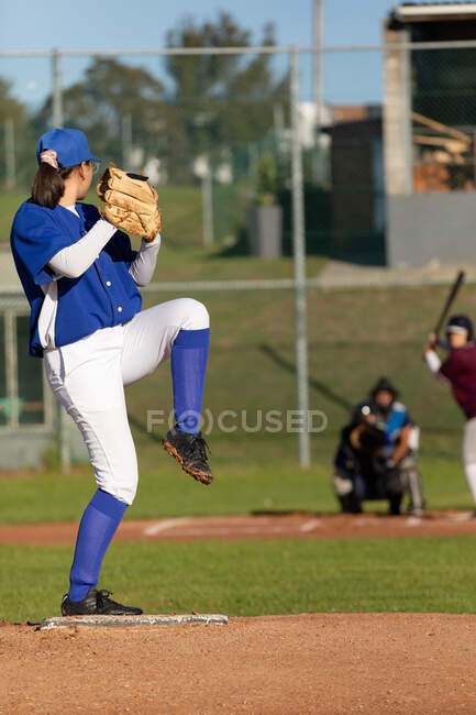Mixed race female baseball pitcher on sunny baseball field preparing to throw ball during game. female baseball team, sports training and game tactics. — Stock Photo