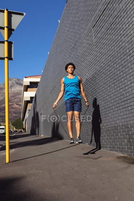 Fit african american man exercising in city jumping with skipping rope in the street. fitness and active urban outdoor lifestyle. — Stock Photo