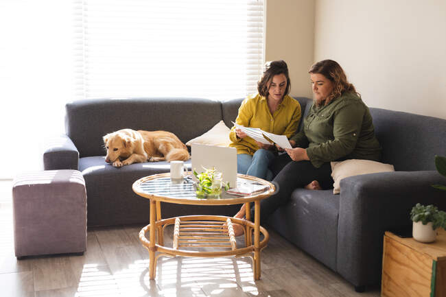 Lesbian couple using laptop and sitting on couch with dog. domestic lifestyle, spending free time at home. — Stock Photo