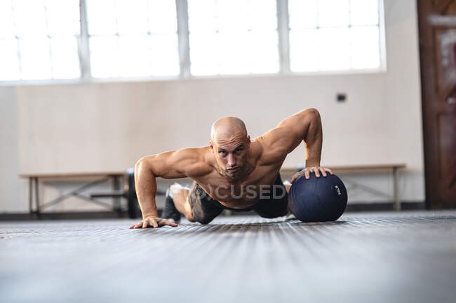 Сильный белый мужчина тренируется в спортзале, отжимается с помощью мяча. силовые и фитнес-кросс тренировки для бокса. — стоковое фото
