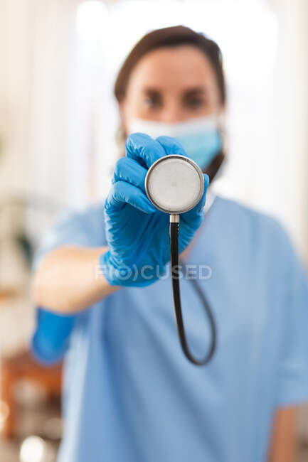 Retrato de médica caucasiana vestindo máscara facial e segurando estetoscópio. serviços médicos e de saúde durante a pandemia do coronavírus covid 19. — Fotografia de Stock