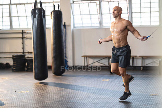 Сильный кавказский мужчина тренируется в спортзале, держит верёвку и прыгает. силовые и фитнес-кросс тренировки для бокса. — стоковое фото