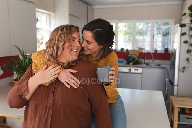 Lesbian couple smiling and drinking coffee in kitchen. domestic lifestyle, spending free time at home. — Stock Photo