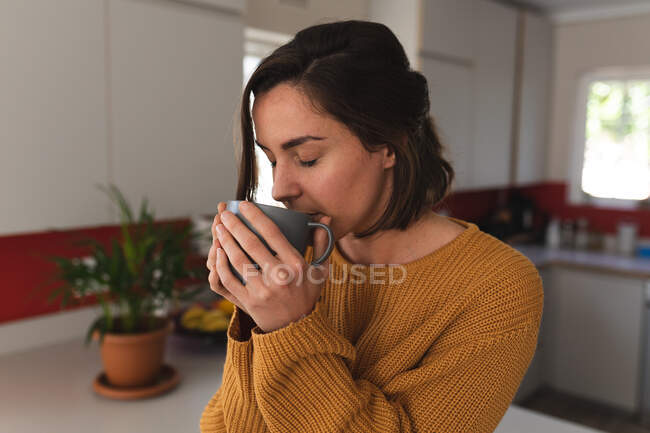 Kaukasische Frau mit geschlossenen Augen trinkt Kaffee in der Küche. häuslicher Lebensstil, Freizeit zu Hause verbringen. — Stockfoto