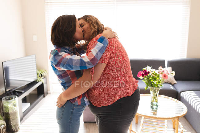 Happy lesbian couple embracing and kissing in living room. domestic lifestyle, spending free time at home. — Stock Photo