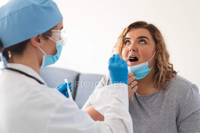 Caucasian female doctor wearing face mask taking swab test from female patient at home. medical and healthcare services home visiting during coronavirus covid 19 pandemic. . medical and healthcare se — Stock Photo