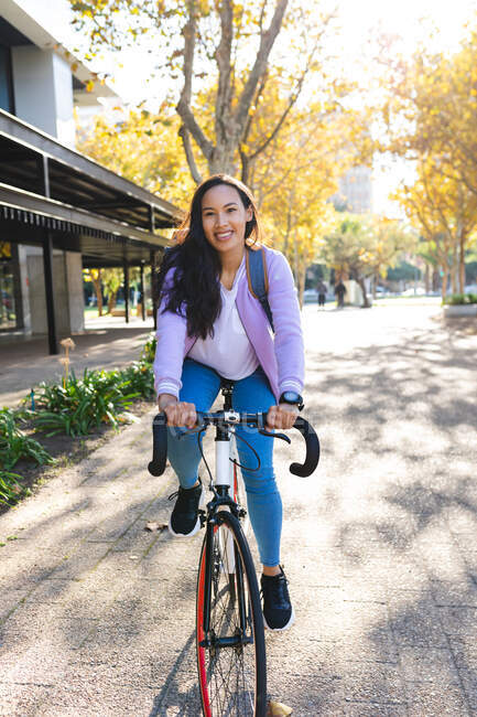 Усміхнена азіатка їде на велосипеді в сонячному парку. незалежна молода жінка на вулиці і близько в місті . — стокове фото