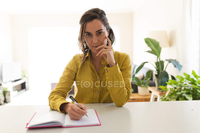 Retrato de mulher caucasiana fazendo uma chamada de vídeo, tomando notas e sorrindo. estilo de vida doméstico, passar o tempo livre em casa. — Fotografia de Stock