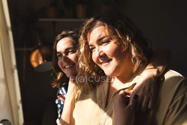 Lesbisches Paar umarmt lächelnd und schaut aus dem Fenster. häuslicher Lebensstil, Freizeit zu Hause verbringen. — Stockfoto