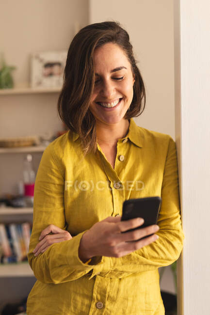 Mujer caucásica vistiendo camisa amarilla y usando smartphone. estilo de vida doméstico, pasar tiempo libre en casa. - foto de stock
