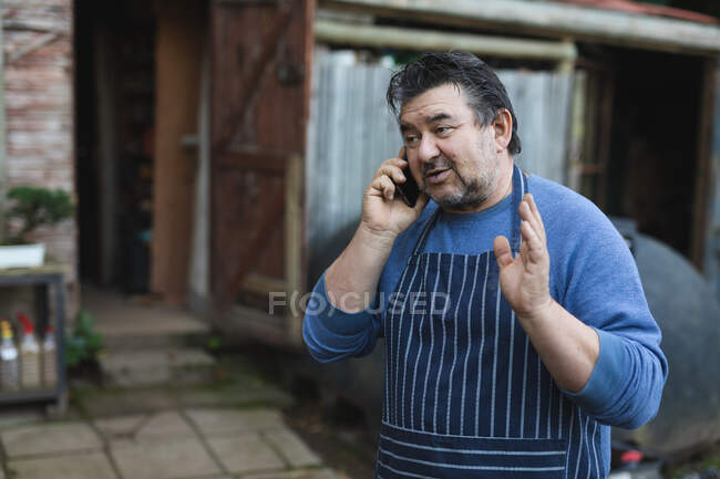 Jardinier masculin caucasien parlant par smartphone au centre de jardin. spécialiste travaillant dans la pépinière de bonsaï, entreprise horticole indépendante. — Photo de stock