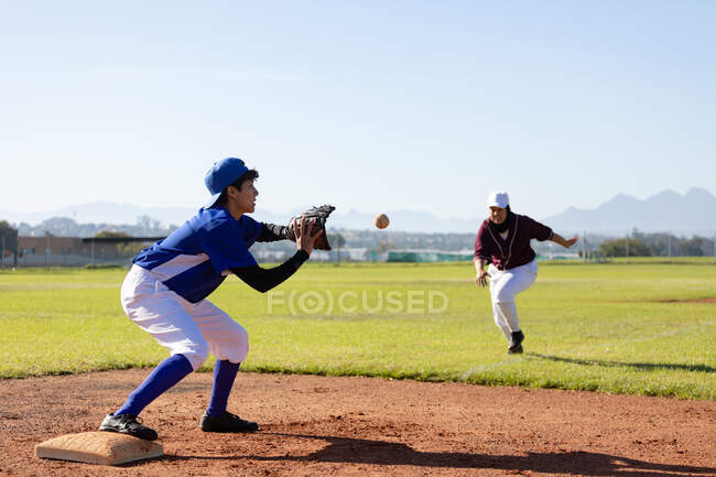 Mixed race female baseball player on sunny baseball field reaching to catch ball during game. female baseball team, sports training and game tactics. — Stock Photo