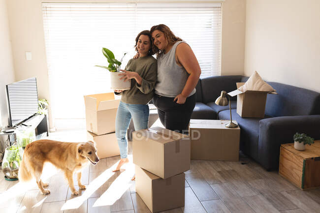 Lesbisches Paar mit Hund lächelt und umarmt sich beim Umzug. häuslicher Lebensstil, Freizeit zu Hause verbringen. — Stockfoto