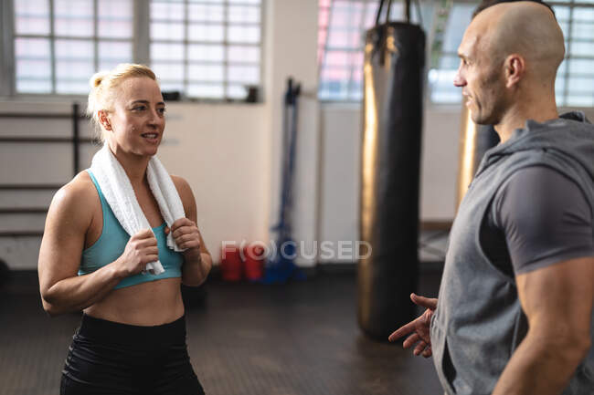 Entraîneur masculin caucasien parlant à une femme exerçant au gymnase. musculation et fitness cross training pour la boxe. — Photo de stock