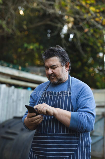 Jardineiro masculino caucasiano usando smartphone no centro do jardim. especialista que trabalha no viveiro de plantas bonsai, negócio de horticultura independente. — Fotografia de Stock