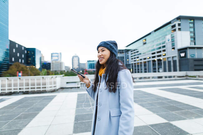Mujer asiática sonriendo y usando smartphone en la calle. mujer joven independiente fuera y alrededor de la ciudad. - foto de stock
