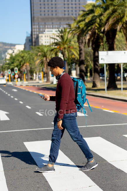 Hombre afroamericano en la ciudad usando smartphone y caminando. nómada digital sobre la marcha, fuera y alrededor de la ciudad. - foto de stock