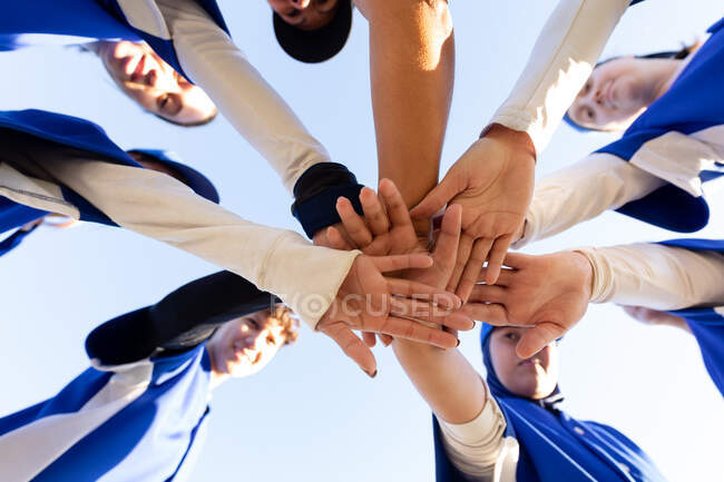 Diverse group of happy female baseball players stacking hands on sunny baseball field before game. female baseball team, sports training, togetherness and commitment. — Stock Photo