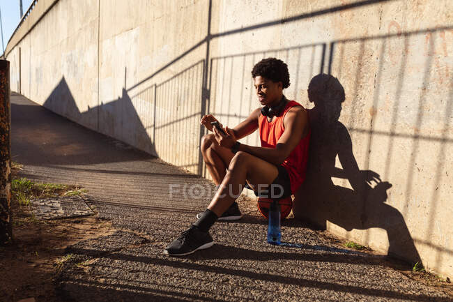 Convient à l'homme afro-américain s'exerçant en ville en utilisant un smartphone dans la rue. forme physique et mode de vie urbain actif. — Photo de stock