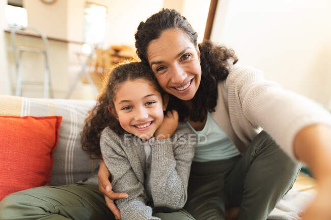 Sorrindo mestiço mãe e filha sentados no sofá tendo videochamada. estilo de vida doméstico e passar tempo de qualidade em casa. — Fotografia de Stock