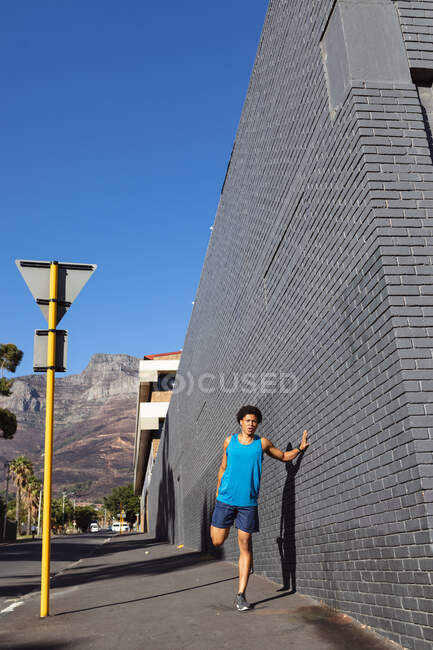 Un uomo afroamericano in forma che si allunga in citta 'per strada. fitness e stile di vita urbano attivo all'aperto. — Foto stock