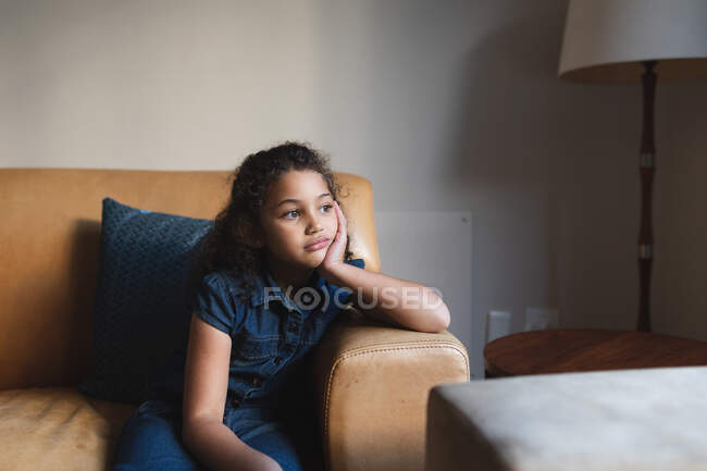 Mixte race fille ennuyée assis sur le canapé dans le salon. style de vie domestique et passer du temps de qualité à la maison. — Photo de stock
