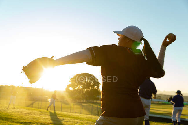 Diverso gruppo di giocatrici di baseball che si scaldano sul campo all'alba, lanciando e prendendo le palle. squadra di baseball femminile, allenamento sportivo estivo. — Foto stock