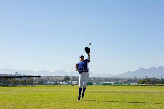 Giocatrice mista di baseball femminile su campo di baseball soleggiato raggiungendo per prendere palla durante la partita. squadra di baseball femminile, allenamento sportivo e tattica di gioco. — Foto stock