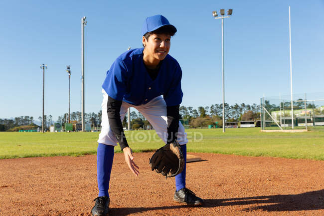 Corrida mista arremessador de beisebol feminino em pé no campo de beisebol ensolarado sorrindo durante o jogo. time de beisebol feminino, treinamento esportivo e táticas de jogo. — Fotografia de Stock