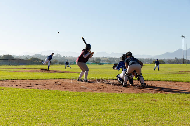 Diverso grupo de jugadoras de béisbol en acción en el campo de béisbol soleado durante el juego. equipo femenino de béisbol, entrenamiento deportivo y tácticas de juego. - foto de stock