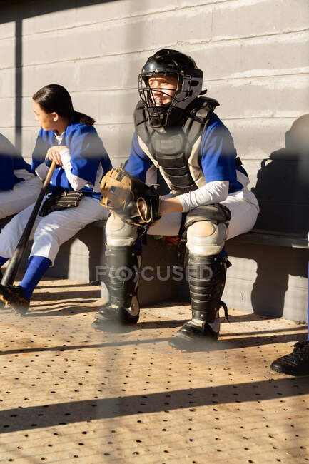 Diverso gruppo di giocatori di baseball femminili seduti in panchina, in attesa di giocare. squadra di baseball femminile, allenamento sportivo, solidarietà e impegno. — Foto stock