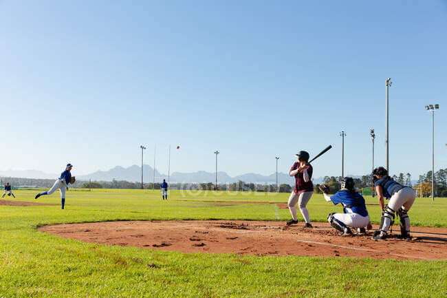 Разнообразная группа женщин-бейсболистов в действии на солнечном бейсбольном поле во время игры. женская бейсбольная команда, спортивная подготовка и тактика игры. — стоковое фото