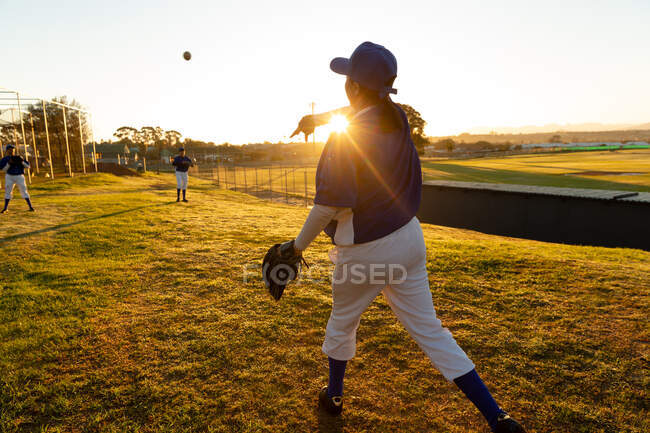 Diverse Baseballspielerinnen wärmen sich bei Sonnenaufgang auf dem Feld auf, werfen und fangen Bälle. Baseballteam der Frauen, Sommersporttraining. — Stockfoto