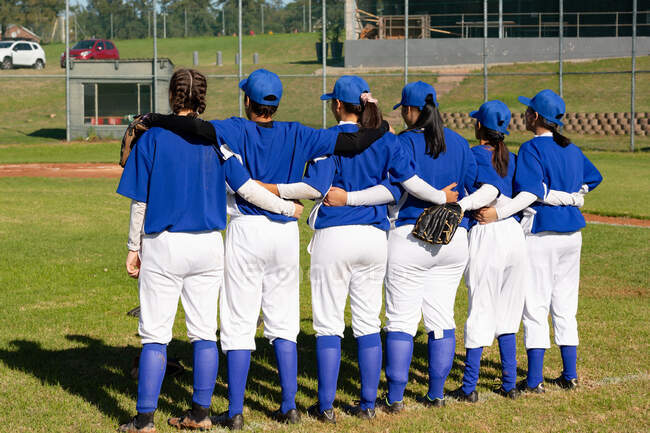 Grupo diverso de jogadoras de beisebol em campo com braços ao redor umas das outras antes do jogo. time de beisebol feminino, treinamento esportivo, união e compromisso. — Fotografia de Stock