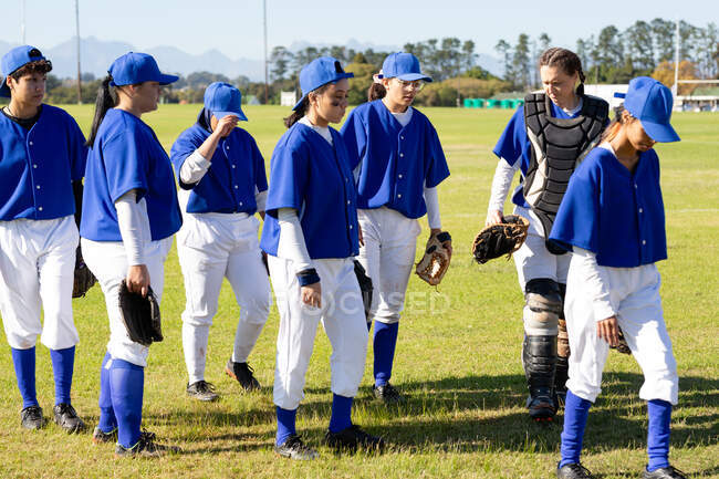 Diverse Baseballspielerinnen gehen nach einem Spiel vom sonnigen Baseballfeld. Baseballmannschaft, Sporttraining, Zusammenhalt und Engagement. — Stockfoto