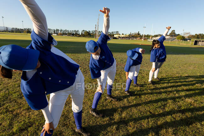 Groupe diversifié de joueuses de baseball s'échauffant sur le terrain, s'étendant de la taille. équipe féminine de baseball, entraînement sportif, convivialité et engagement. — Photo de stock