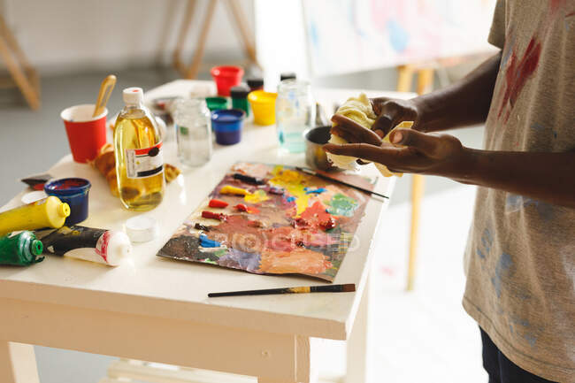 Pittore afroamericano di sesso maschile al lavoro che pulisce le mani nello studio d'arte. creazione e ispirazione in uno studio di pittura artisti. — Foto stock