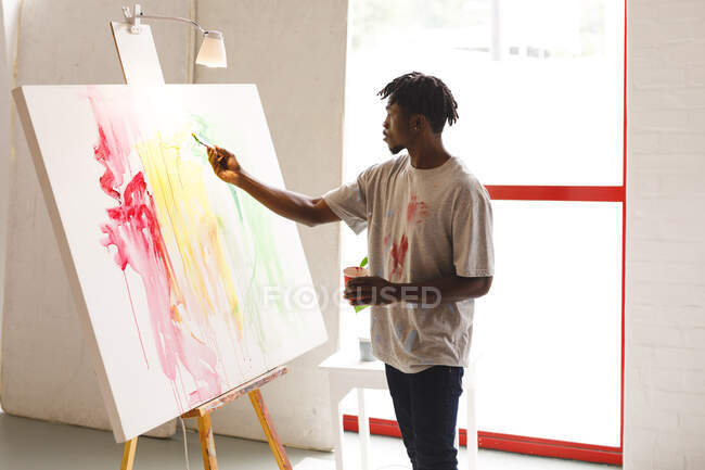 Pintor masculino afroamericano trabajando pintando sobre lienzo en estudio de arte. creación e inspiración en un estudio de pintura de artistas. - foto de stock