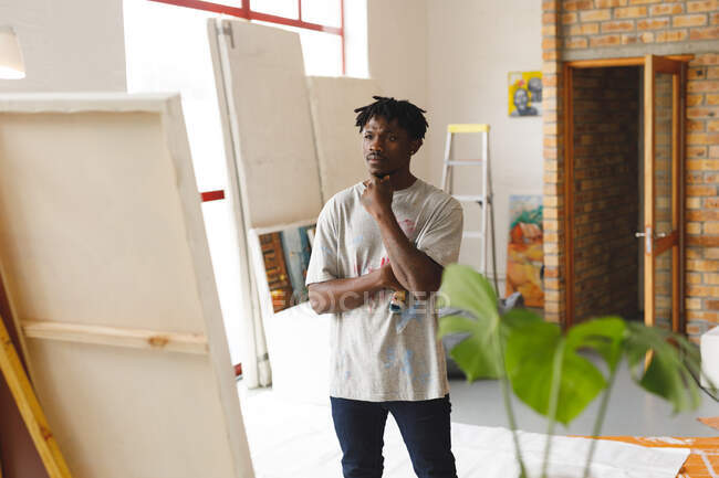 African american male painter at work looking at artwork in art studio. creation and inspiration at an artists painting studio. — Stock Photo