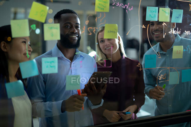 Divers collègues d'affaires masculins et féminins lisant des notes de service colorées sur un mur de verre. travailler en entreprise dans un bureau moderne. — Photo de stock