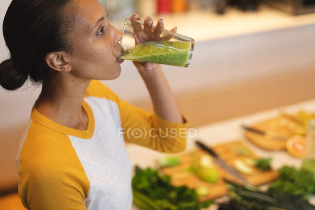 Mixed race woman in kitchen drinking health drink. domestic lifestyle, enjoying leisure time at home. — Stock Photo