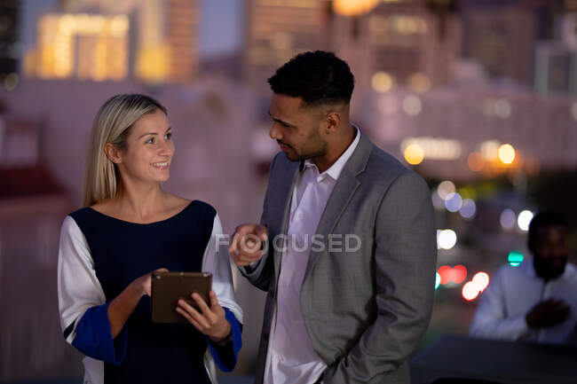 Diverse male and female business colleagues working at night using tablet and talking. working late in business at a modern office. — Stock Photo