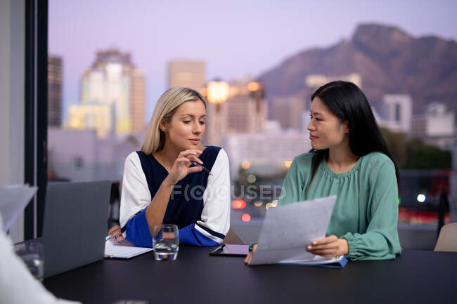 Двоє різних бізнес-колег жінок розмовляють і тримають документи. робота в бізнесі в сучасному офісі . — стокове фото