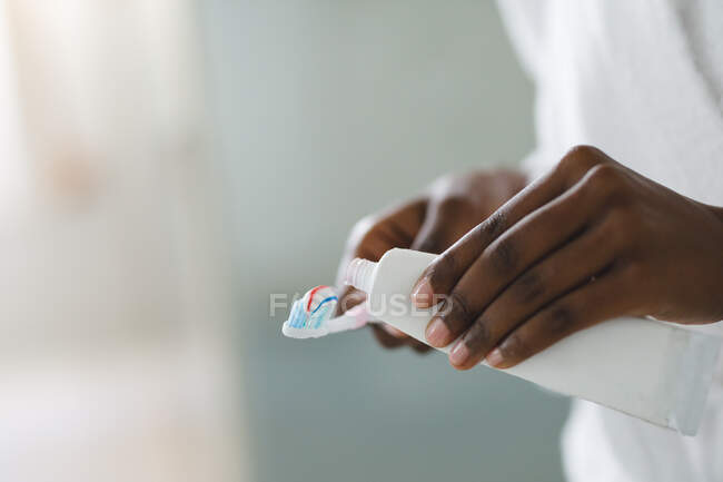 Close up of african american woman in bathroom holding toothpaste and toothbrush. domestic lifestyle, enjoying leisure time at home. — Stock Photo