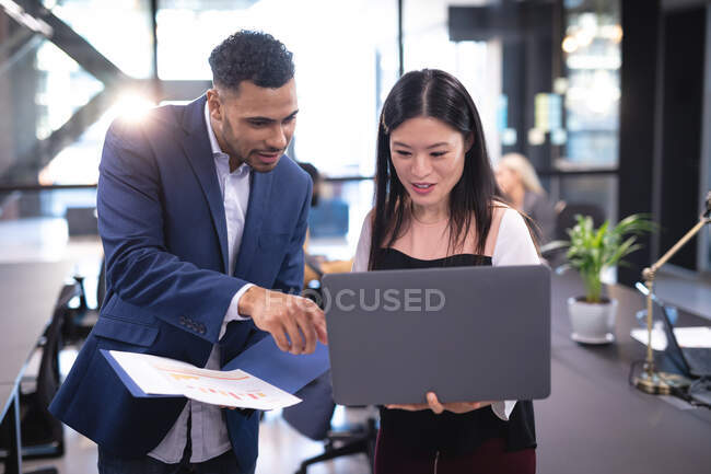 Two diverse male and female business colleagues using laptop and talking. working in business at a modern office. — Stock Photo