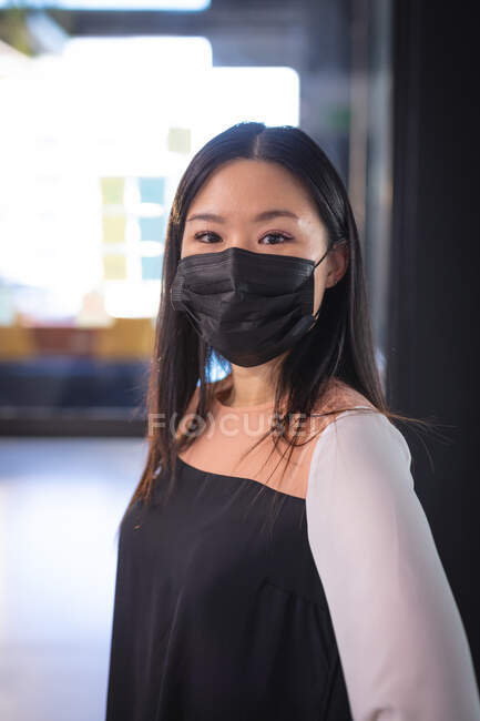 Porträt einer asiatischen Geschäftsfrau mit Gesichtsmaske und Blick in die Kamera. Arbeit in einem modernen Büro während der Coronavirus-Pandemie 19. — Stockfoto