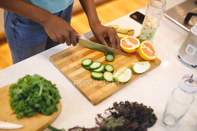 Африканская американка на кухне режет овощи и фрукты. домашний образ жизни, наслаждаясь отдыхом дома. — стоковое фото