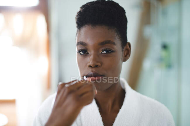 Portrait of african american woman in bathroom brushing teeth. domestic lifestyle, enjoying leisure time at home. — Stock Photo